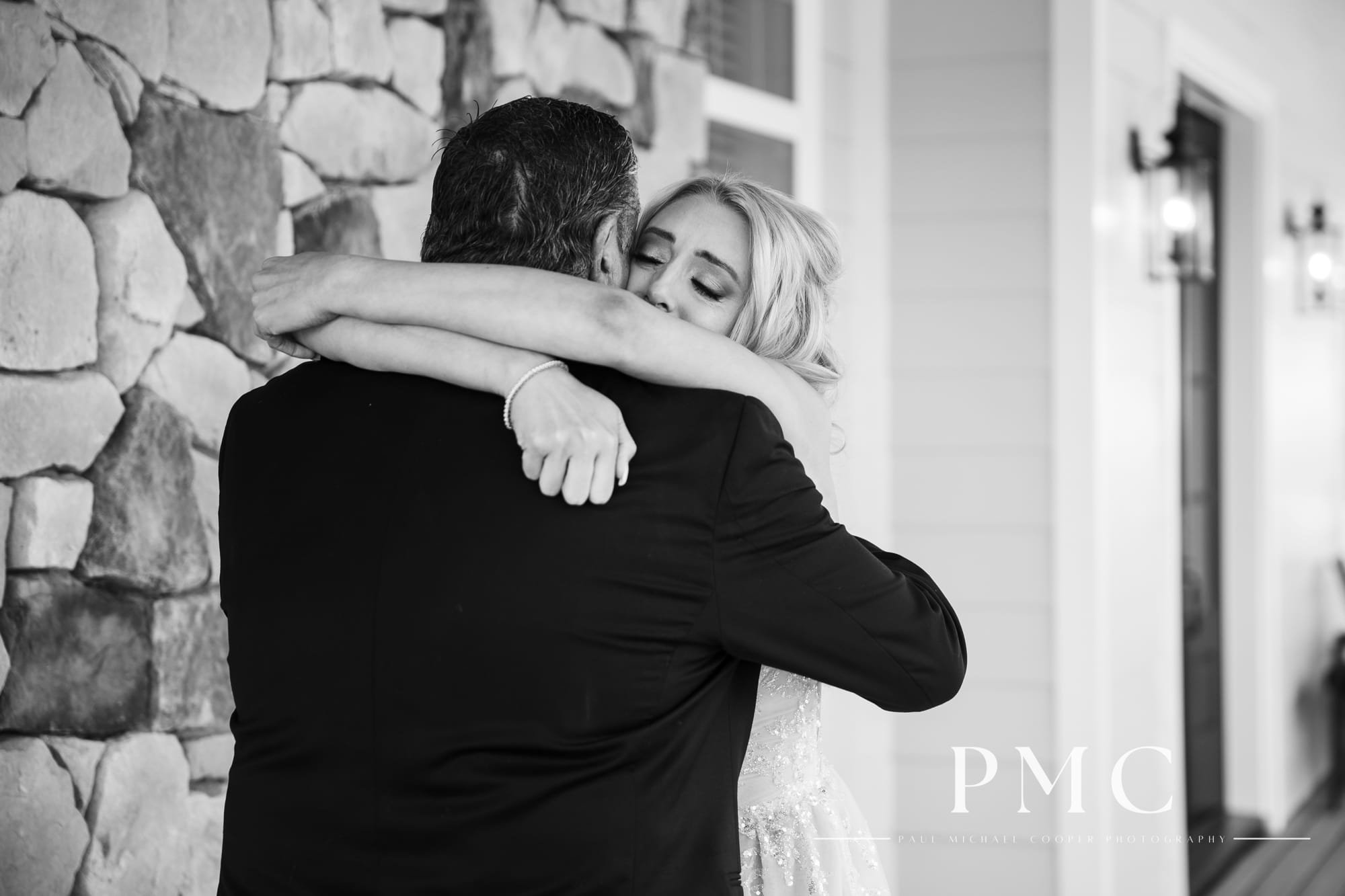 A bride shares a touching First Look with her father on the porch of a ranch house on the day of her wedding with a black-and-white wedding theme.