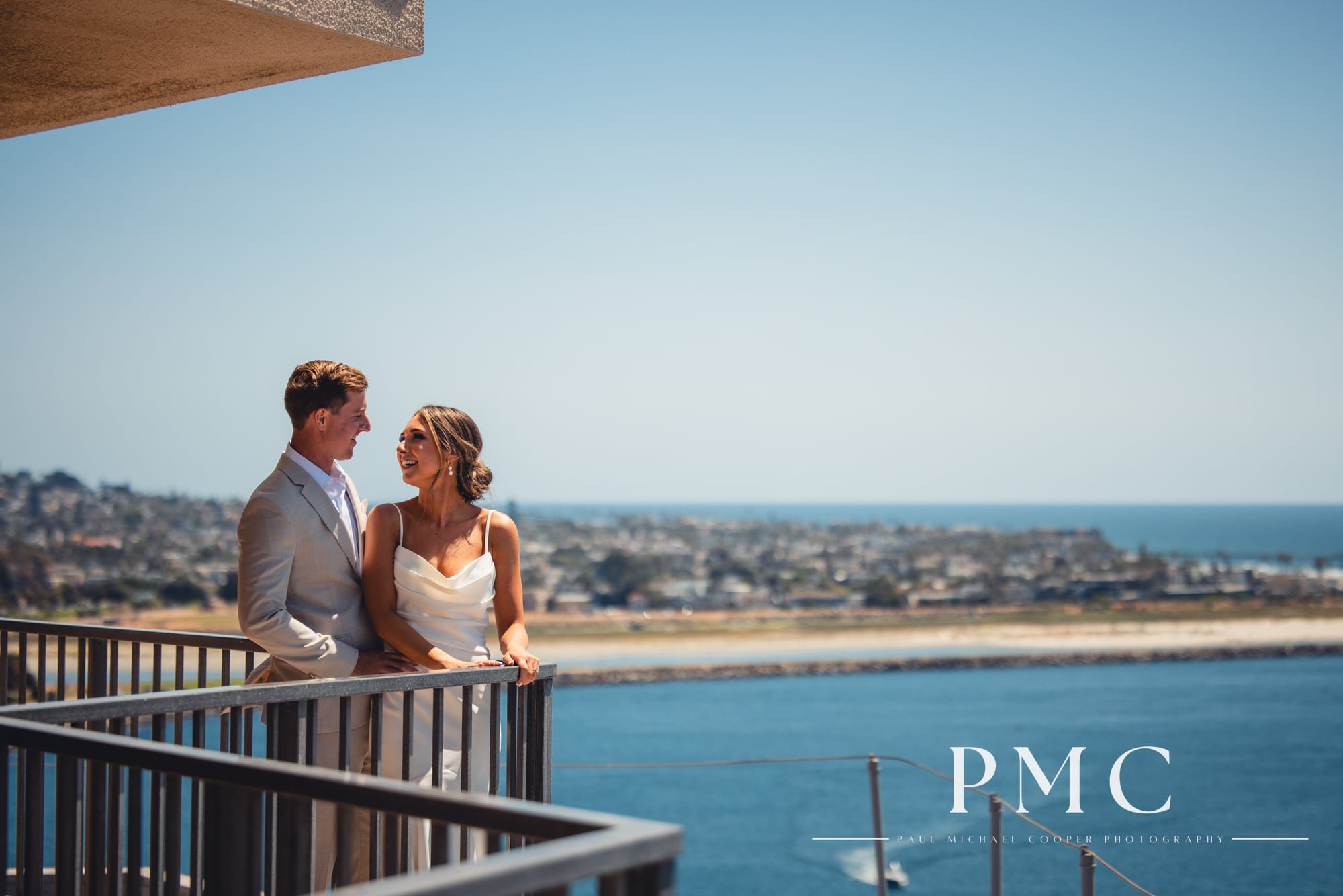 A bride and groom smile at each other on the balcony of the Hyatt Regency Mission Bay Resort on their wedding day.