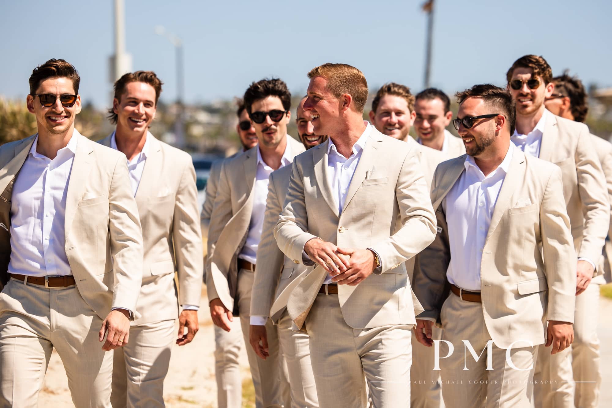 A groom and his groomsmen walk and smile at each other on the beach in Mission Bay.