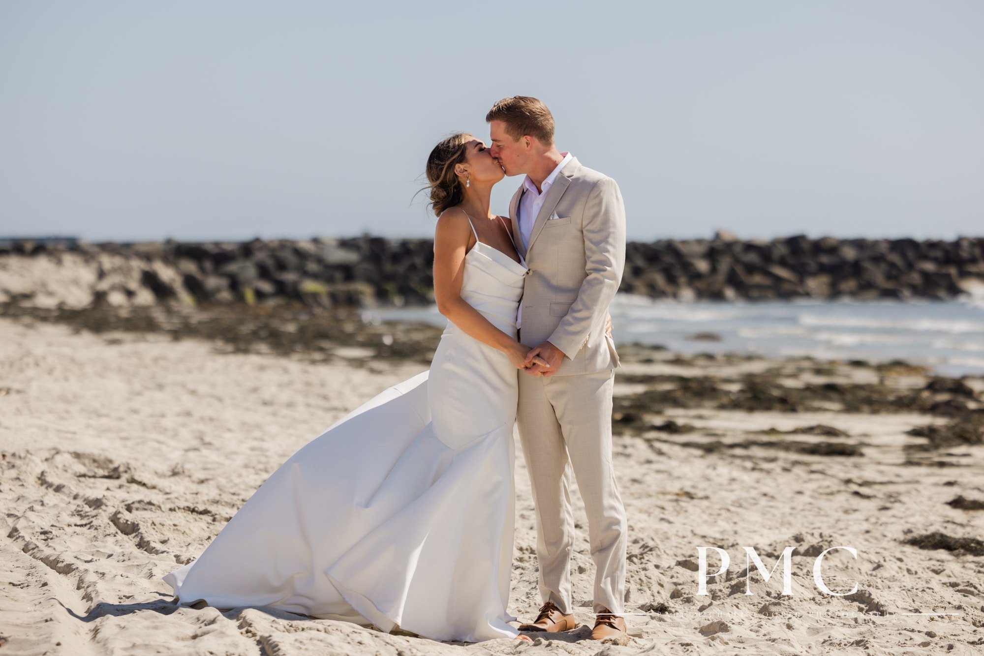 A bride and groom hold hands and kiss on the beach in Mission Bay.