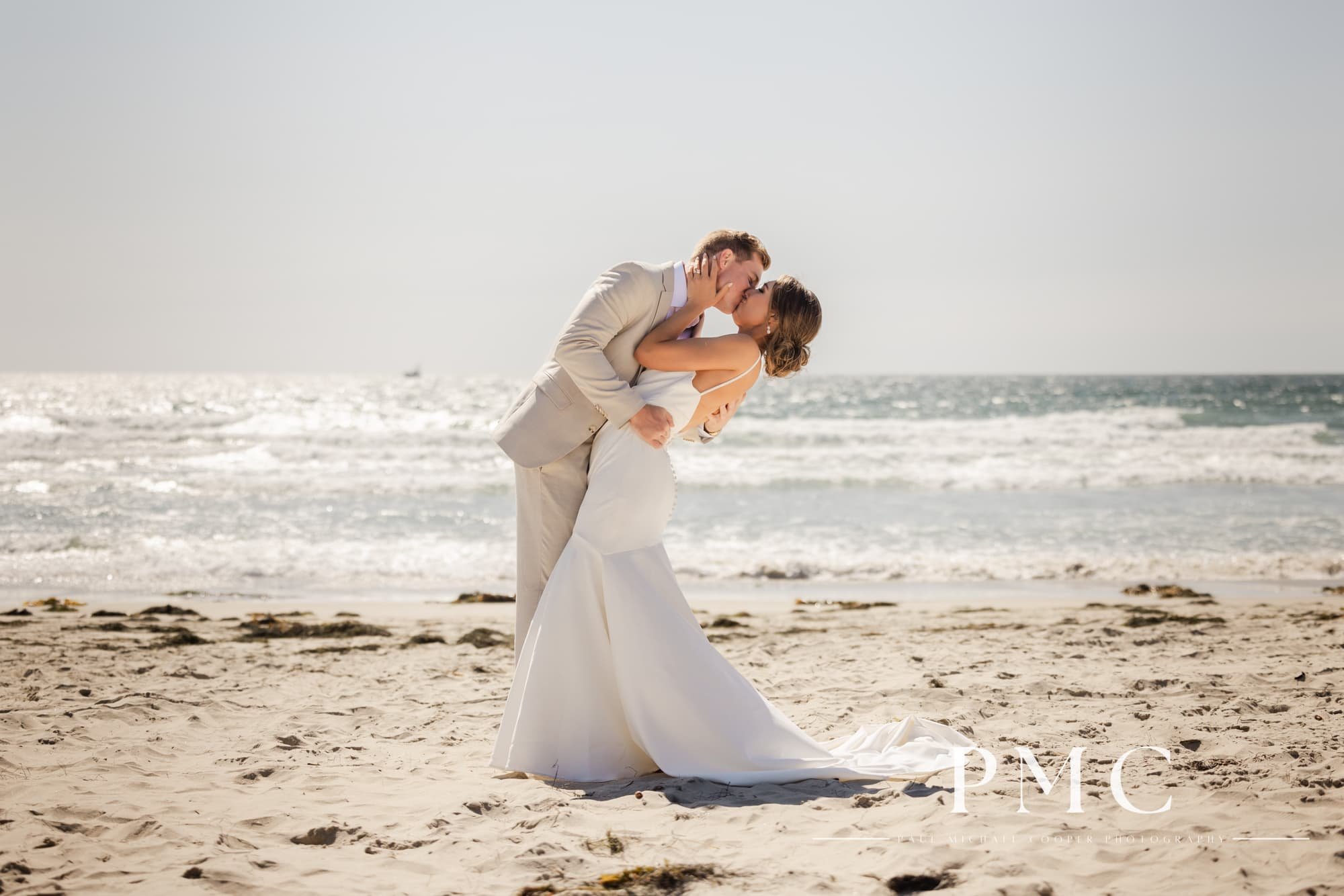 A bride and groom kiss on the beach in Mission Bay.