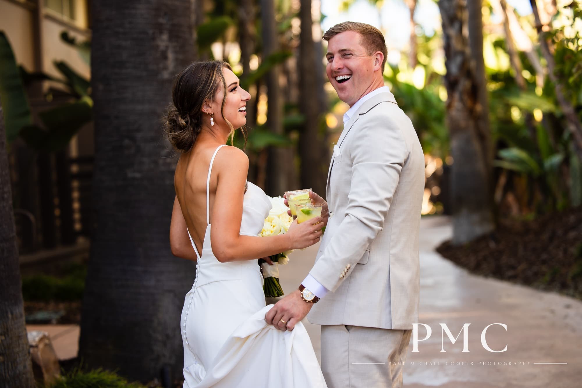 A bride and groom smile as they walk through the Hyatt Regency Mission Bay Resort with their cocktails in their hands.