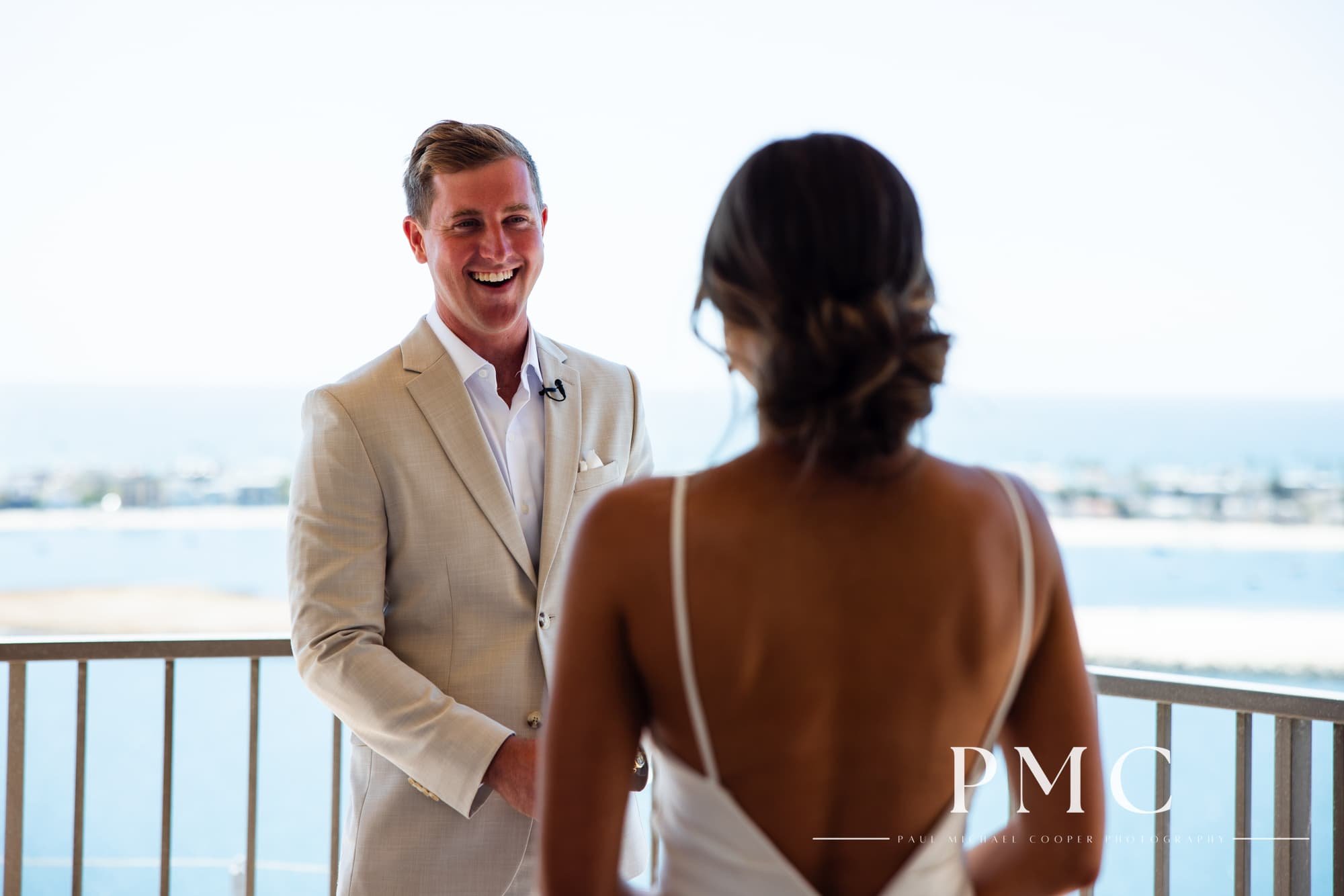 A groom smiles wide at his bride during their wedding day first look on the balcony of the Hyatt Regency Mission Bay.