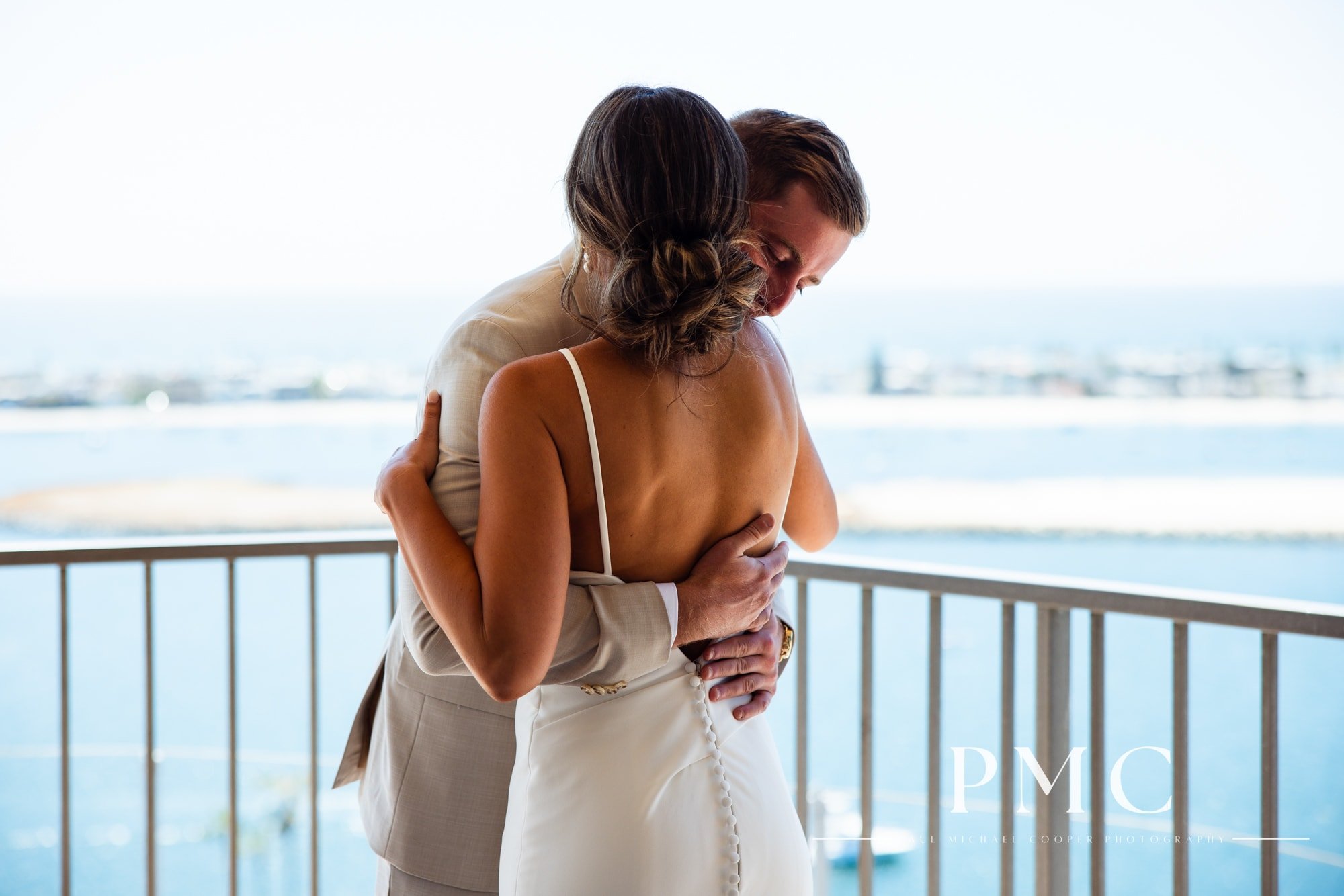 A groom hugs his bride during their wedding day first look on the balcony of the Hyatt Regency Mission Bay.