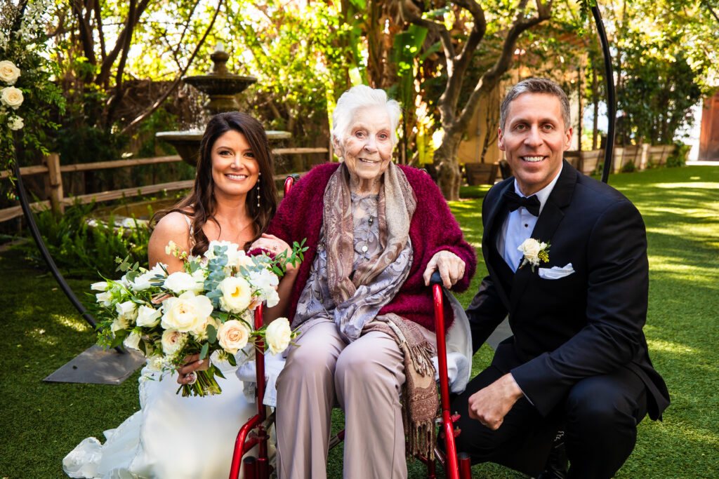 A bride and groom take a photo with the bride's grandmother, a guest of honor at their outdoor spring wedding.