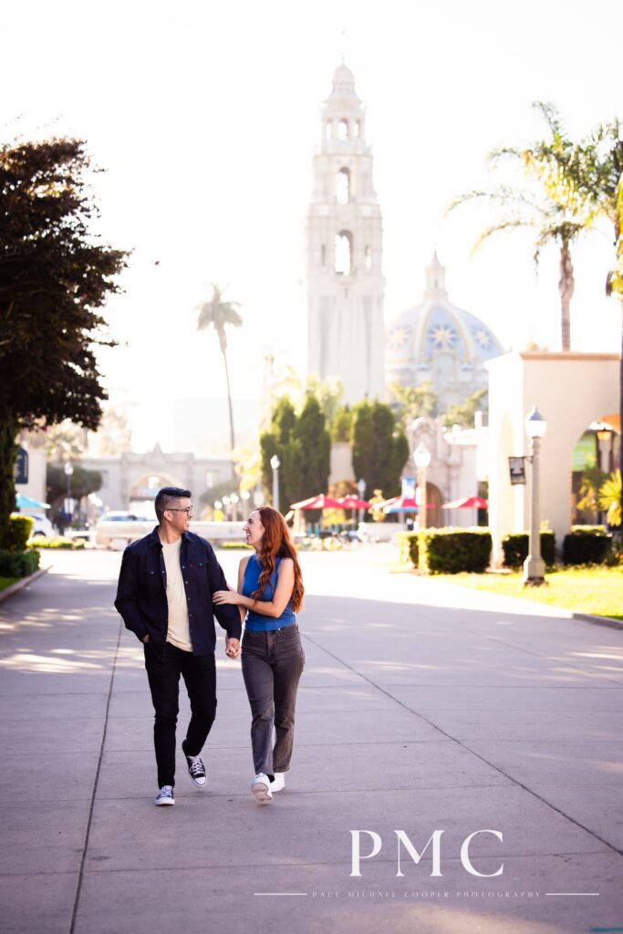A couple smiles and hold hands during their Balboa Park engagement session.