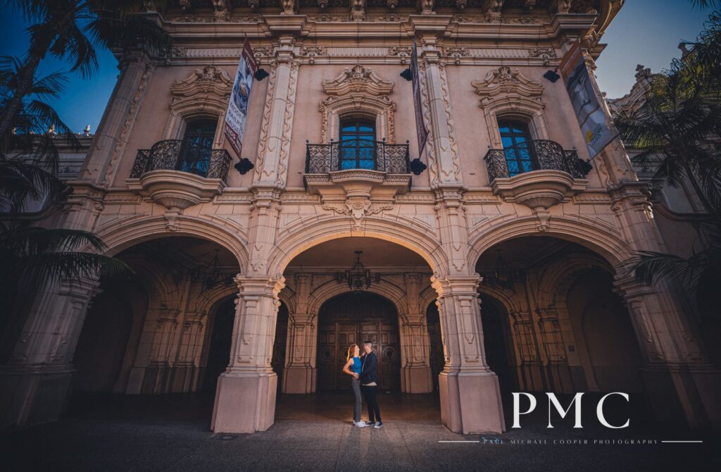 A cinematic portrait of a couple and an impressive building during their Balboa Park engagement session.