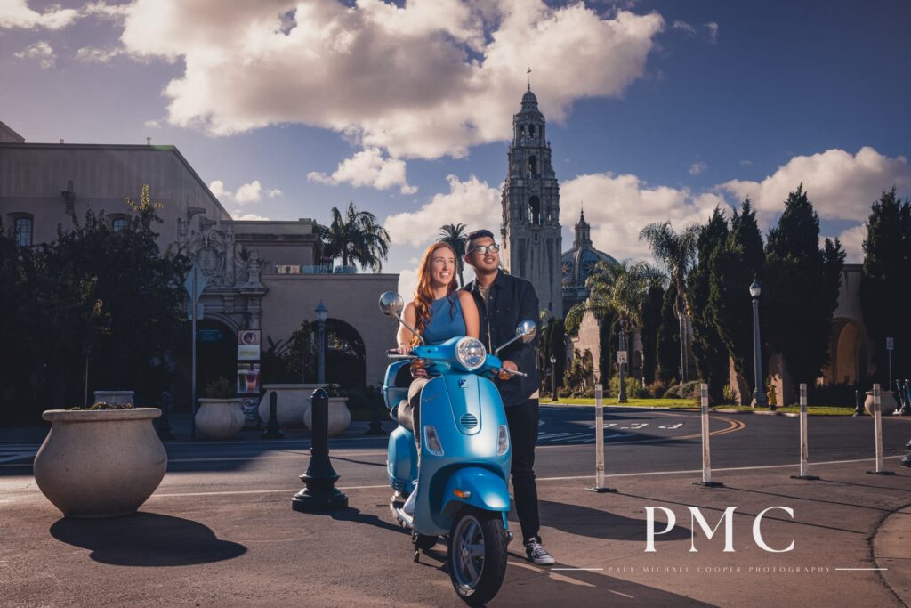 A couple smile on their blue Vespa during their Balboa Park engagement session.