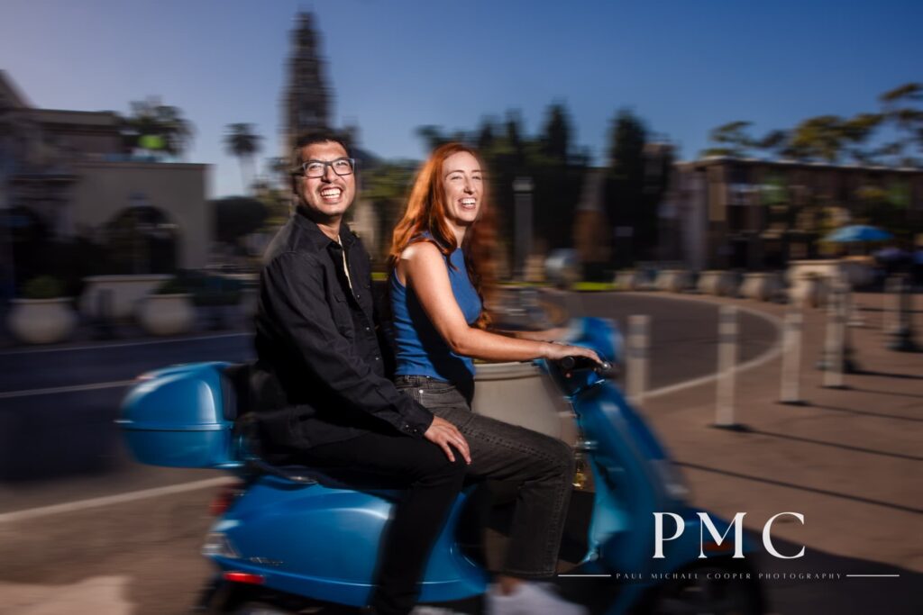 A couple smile on their blue Vespa during their Balboa Park engagement session.