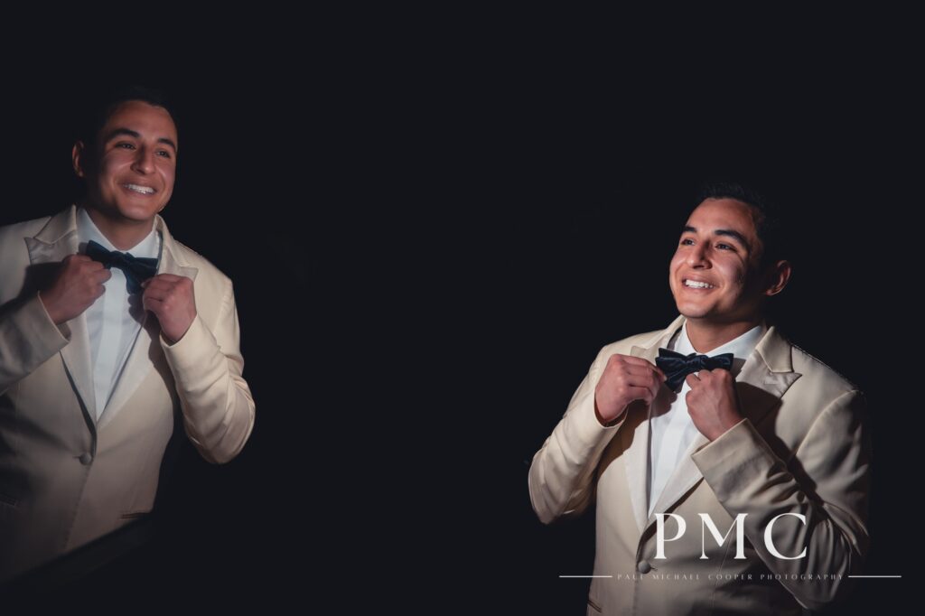 A groom smiles and straightens his bow tie.