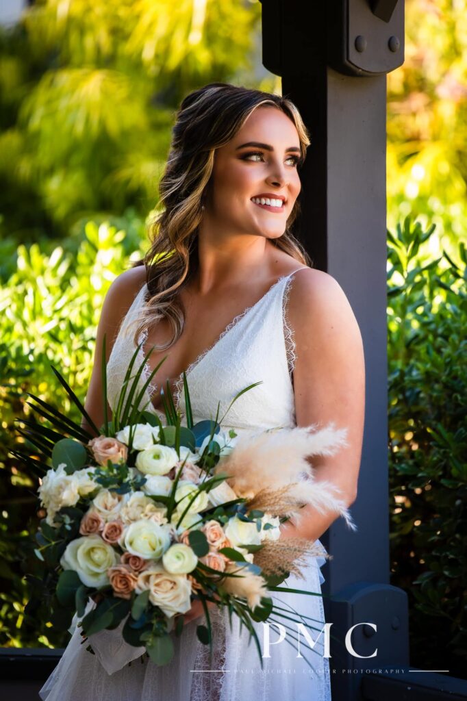 A bride smiles and holds her bouquet in a gazebo on her spring wedding day.