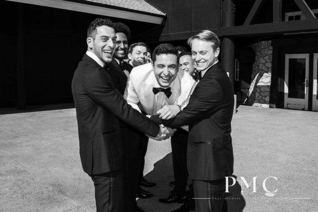 Black and white wedding photo of a laughing groom being held up by his groomsmen.