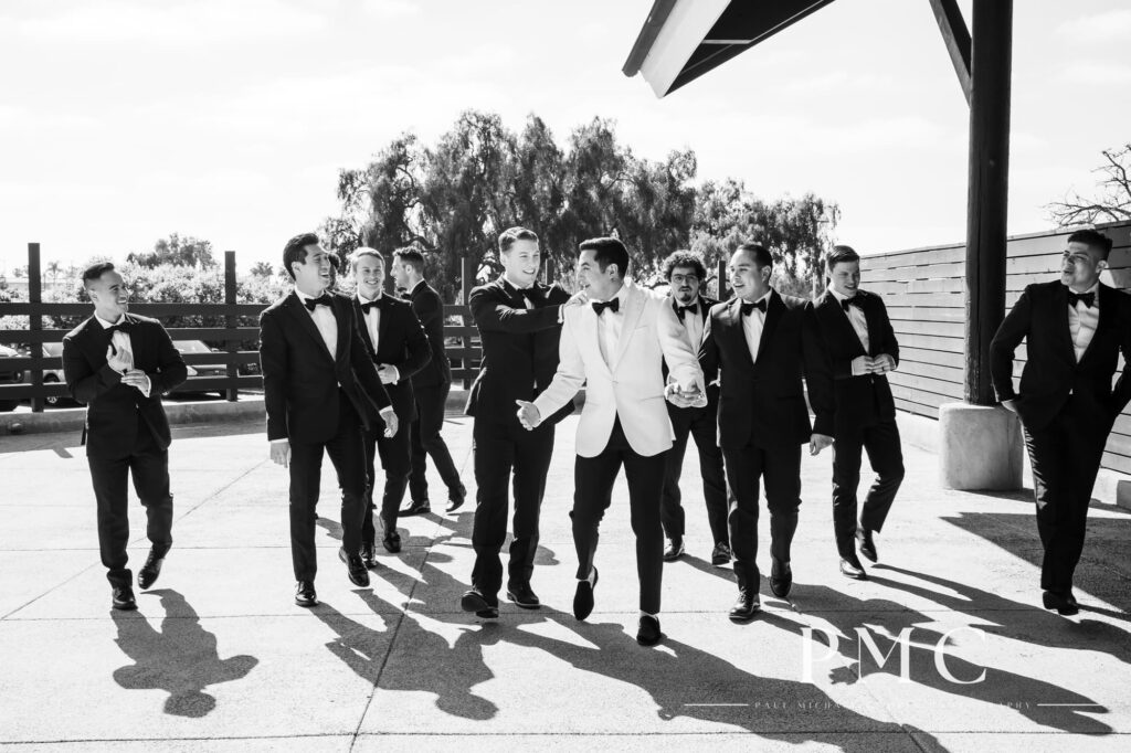 A groom and his groomsmen walk and celebrate together in this black and white wedding photo.