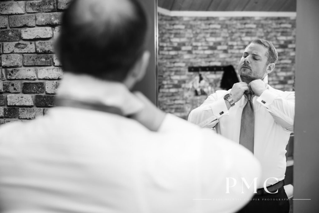 A groom adjusts his tie before his wedding ceremony.