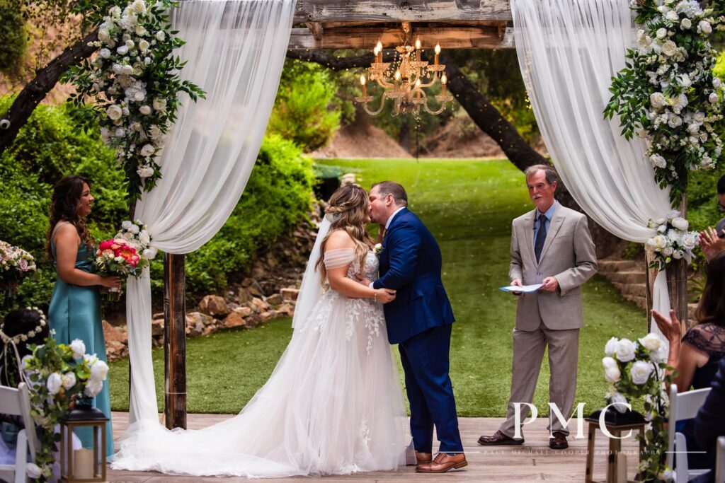 A bride and groom share their first kiss as husband and wife at their outdoor summer wedding ceremony.