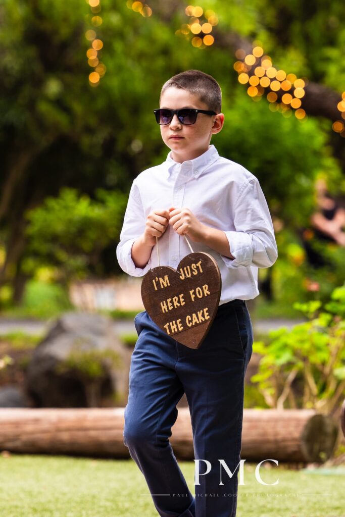 A junior groomsman enters the ceremony carrying a sign that reads, "I'm just here for the cake."