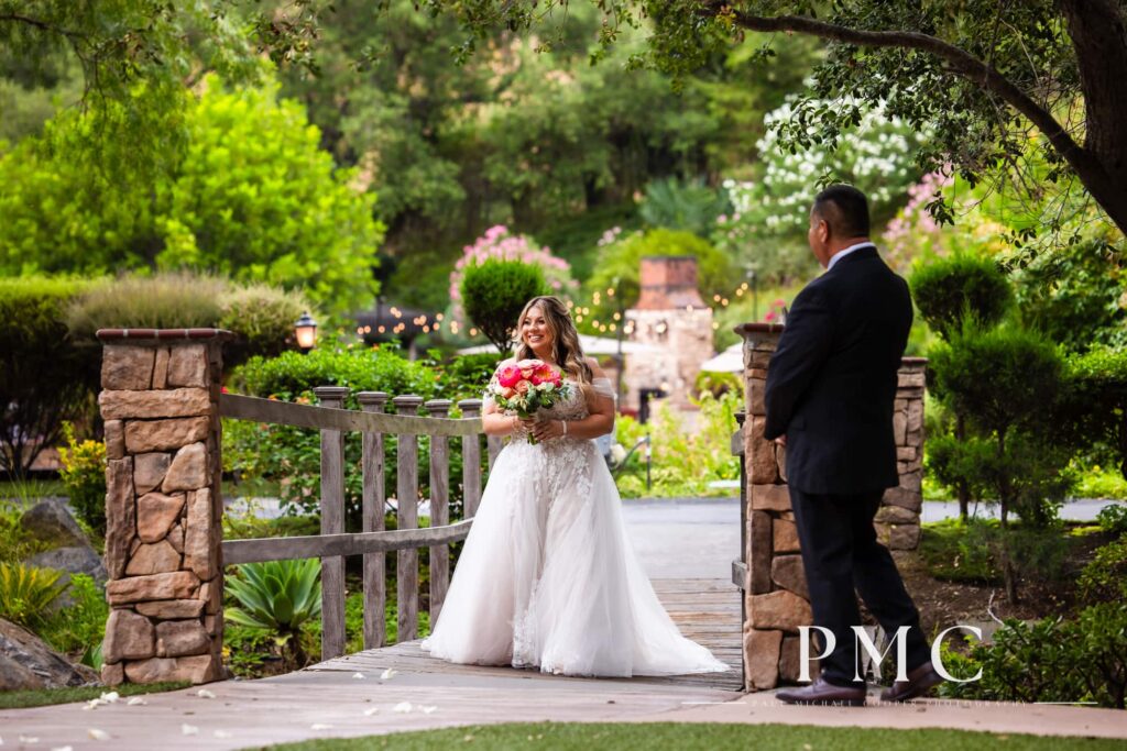 A bride with a vibrant floral bouquet smiles widely as she enters her outdoor summer wedding ceremony.