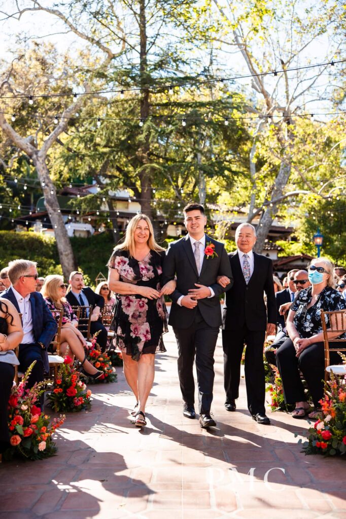 A groom escorts his parents down the aisle at his outdoor spring wedding.