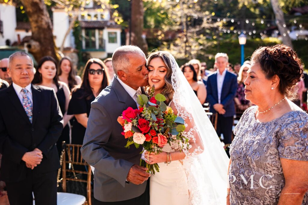 A bride receives a kiss on her cheek from her father as he gives her away at the altar at her outdoor spring wedding.