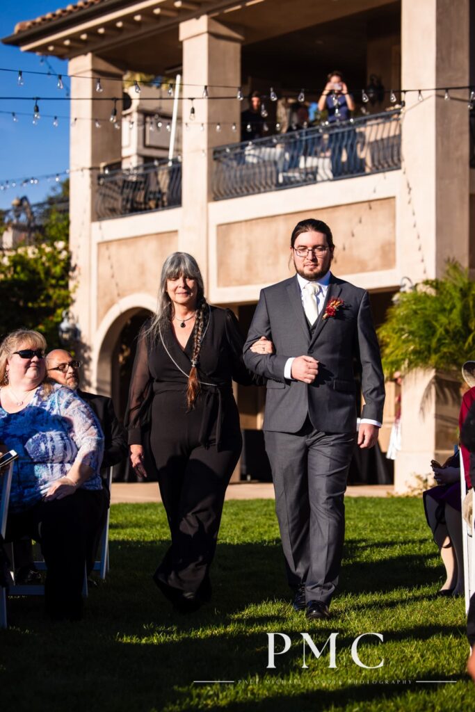 The groom escorts his mother down the aisle at his fall wedding on a private estate in Escondido.