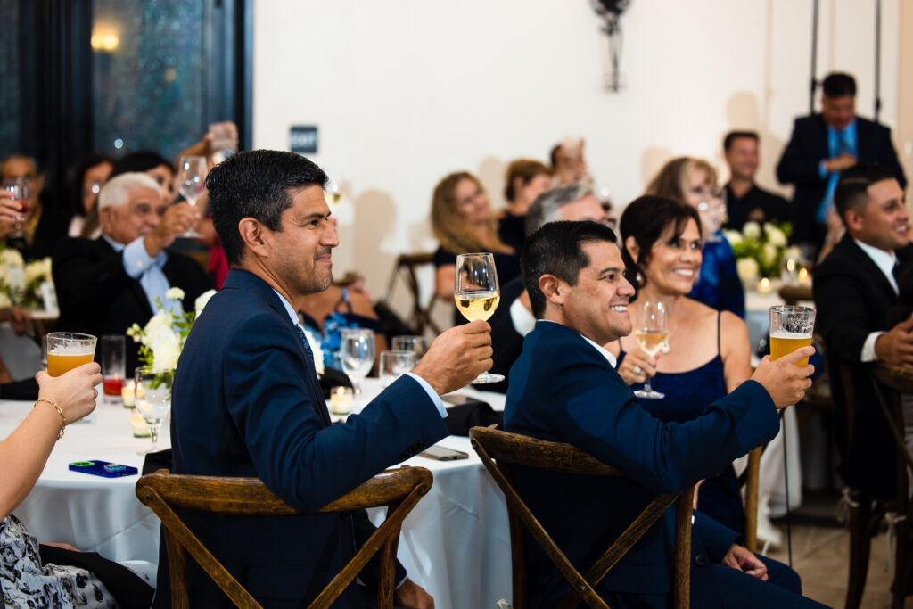 Wedding guests seated and raising their glasses in a toast at an indoor wedding reception at Avensole Winery in Temecula.