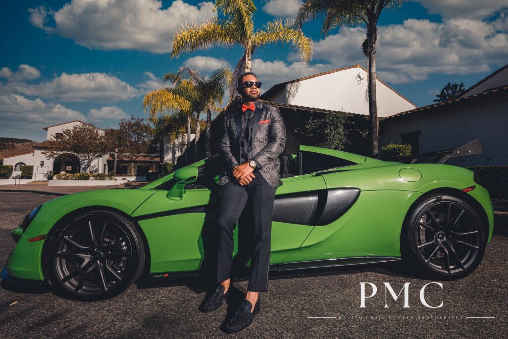A stylish groom poses in front of a bright green McLaren wedding car.