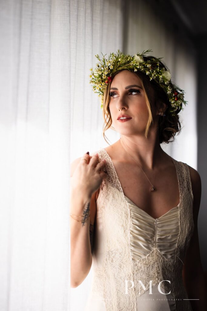 A bride wears her grandmother's vintage wedding dress and boho floral crown by a window.