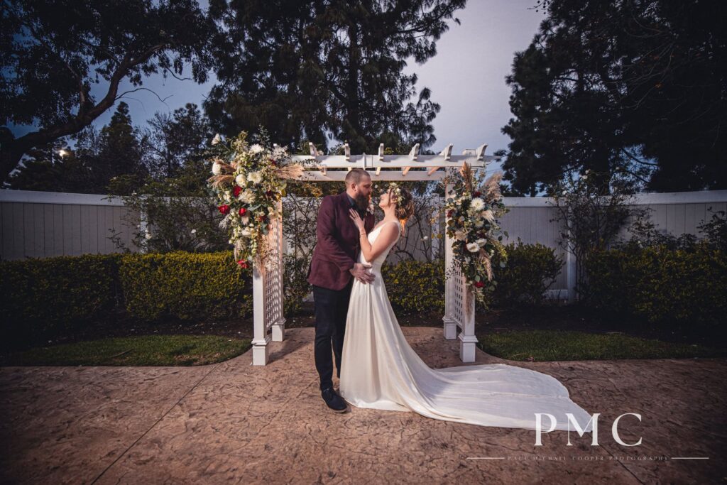A cinematic portrait of a bride and groom embracing in front of their wedding arch with boho-inspired florals.