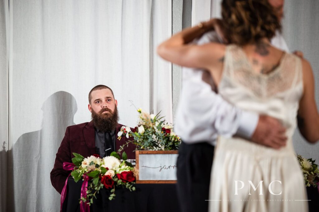 A groom watches his bride share the Father-Daughter dance with her father on their wedding day.