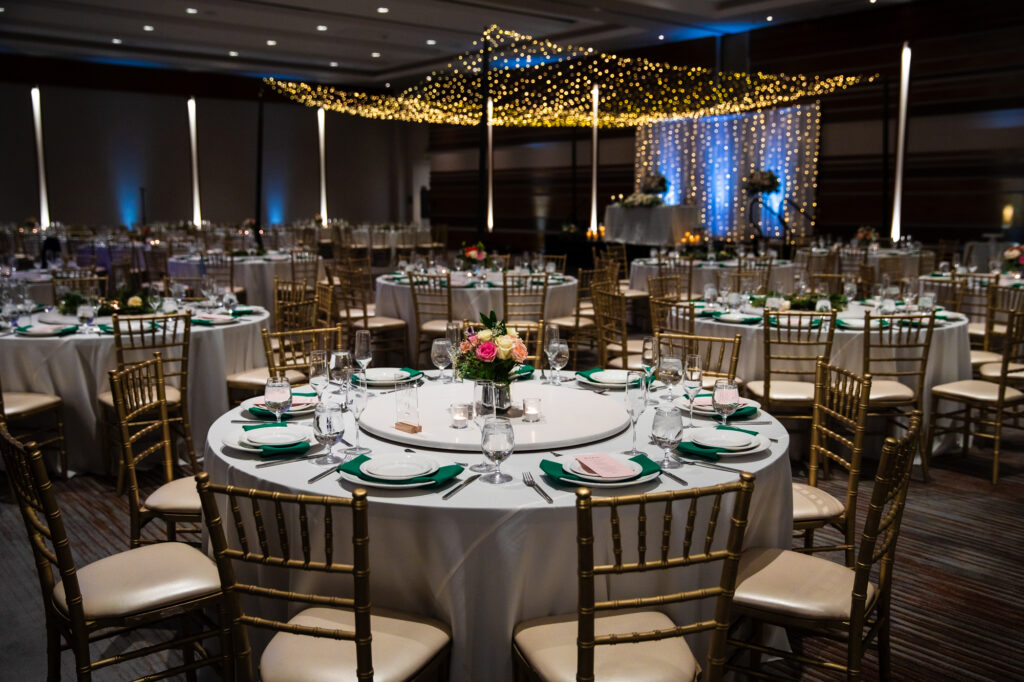 Round tables, linens, and florals set up for wedding seating at a winter wedding reception with fairy lights in the background.