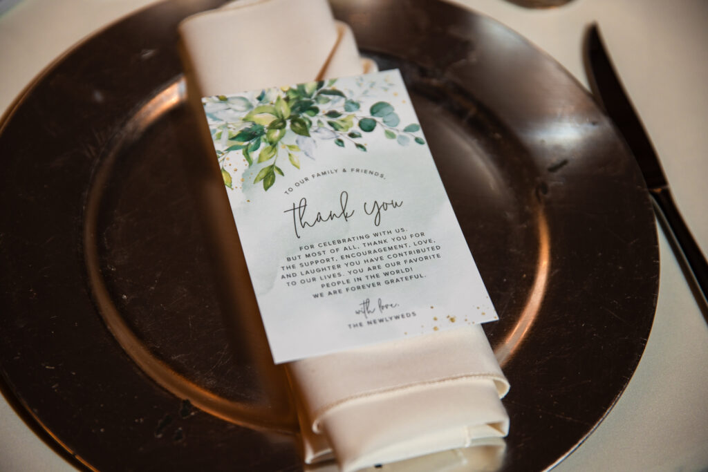 A thank you note from the newlyweds sits on top of the guests' linens at their wedding seating arrangement at the wedding reception.