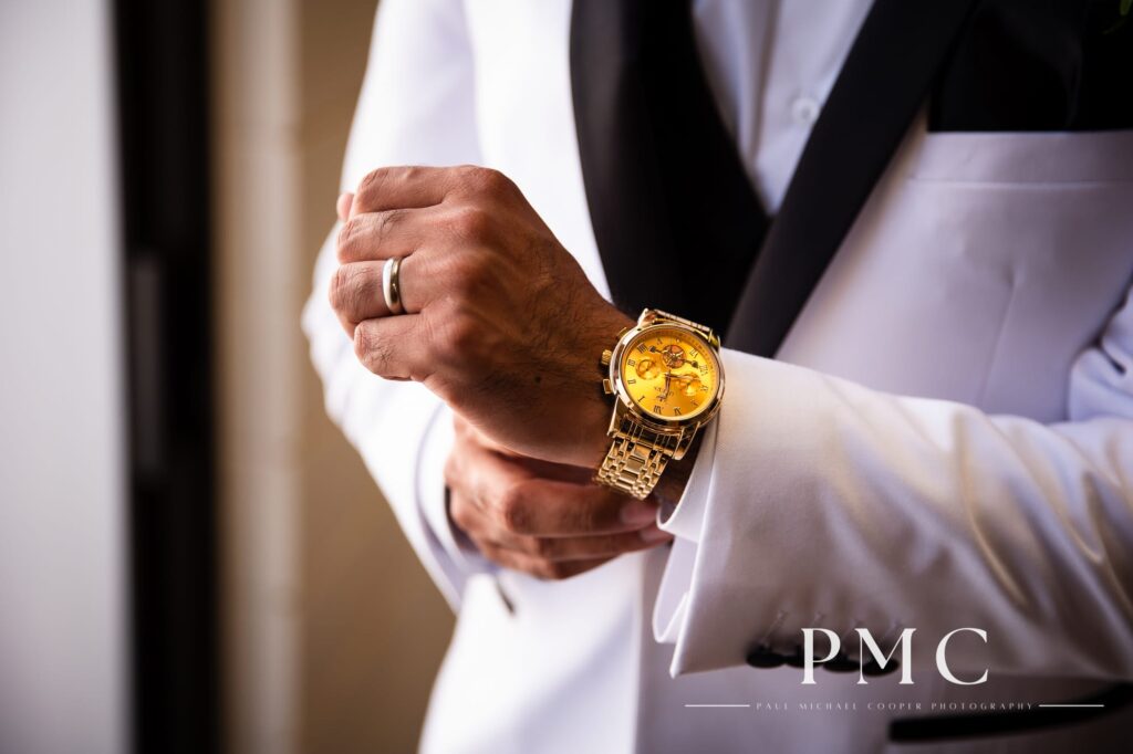 Close-up photo of a groom's gold watch and white suit jacket.