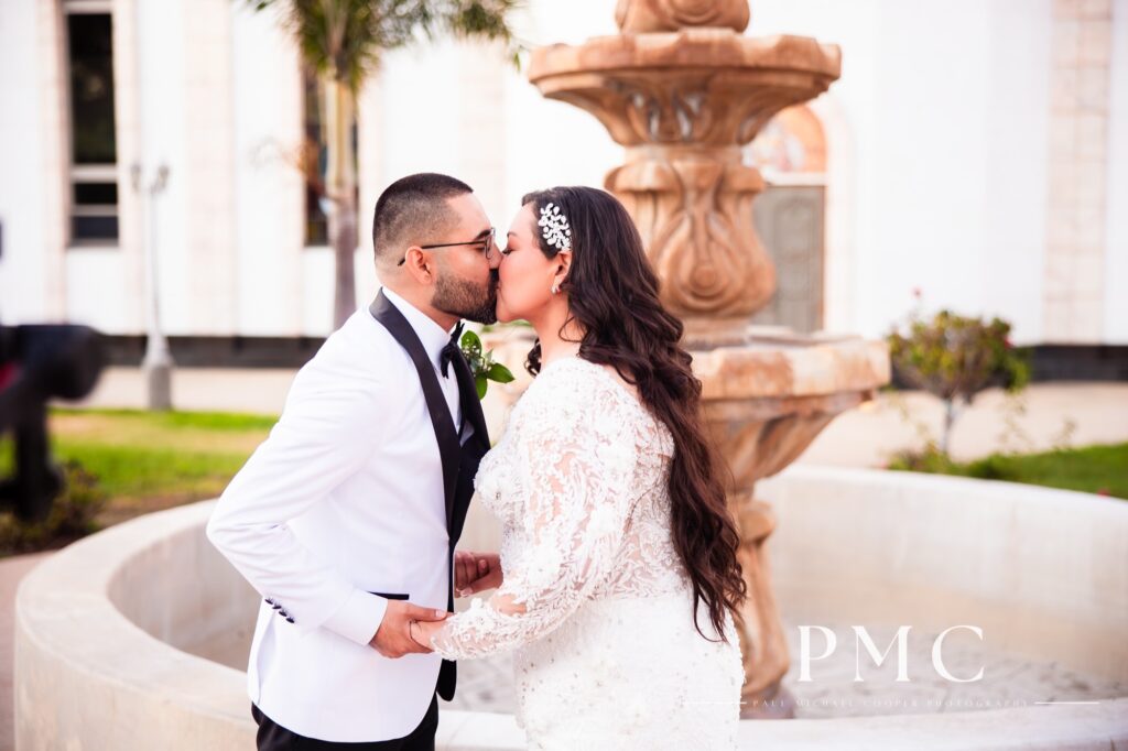 A bride and groom share a kiss in front of a church fountain on their San Diego wedding day.