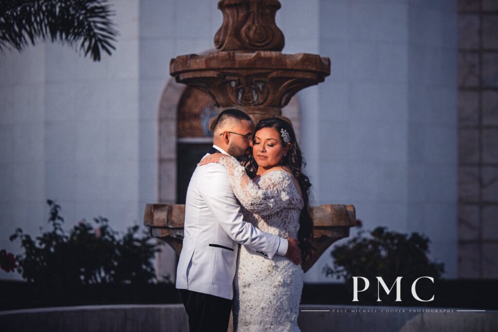 A bride and groom share a kiss in front of a church fountain on their San Diego wedding day.