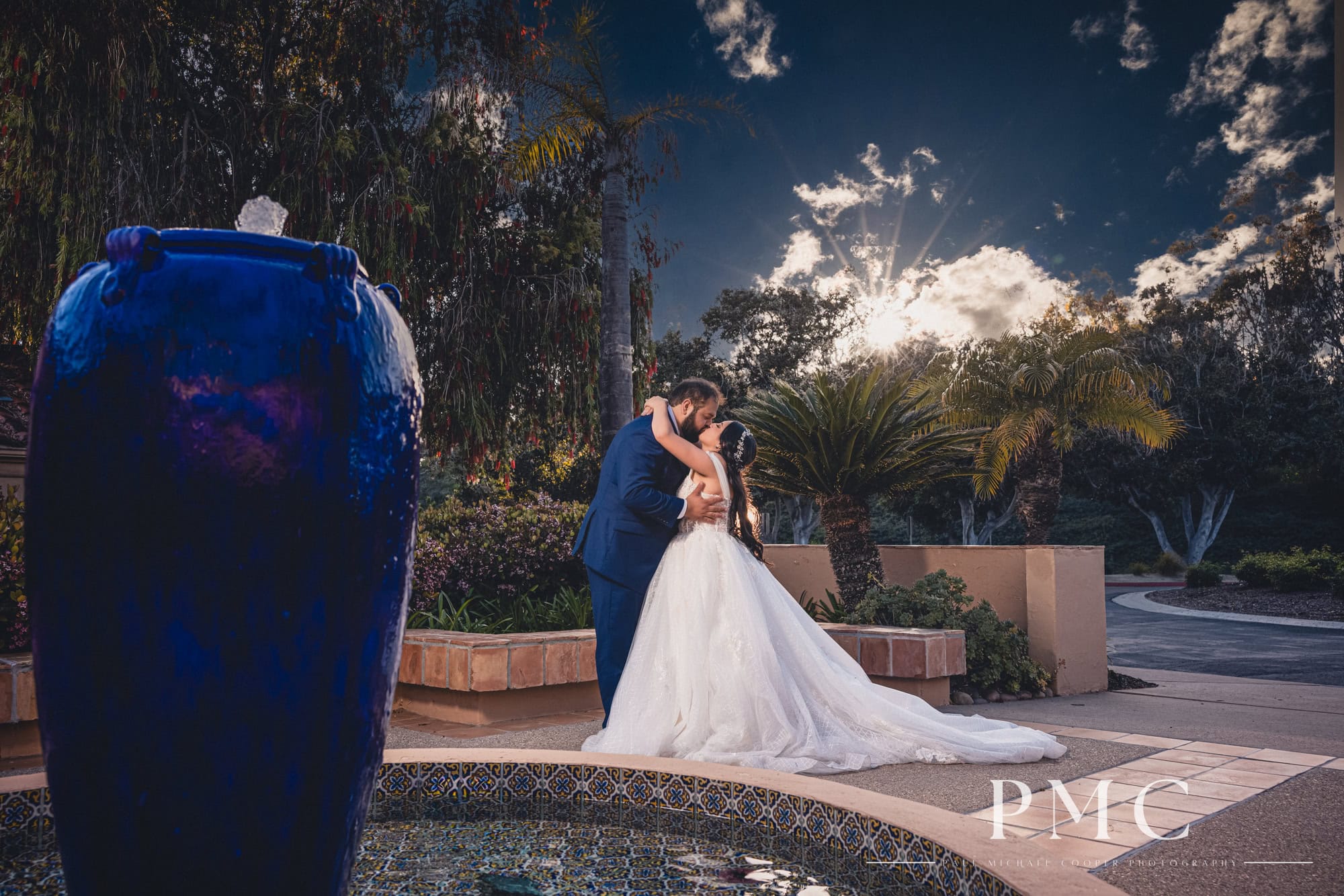 A bride and groom share an embrace and kiss at sunset at the front fountain of The Heights Golf Course.