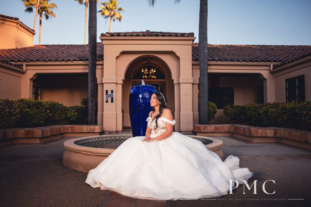 A bride sits and smiles at the fountain at the front entrance of The Heights Golf Course.