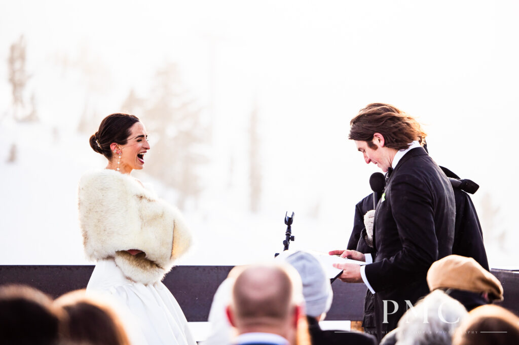 A bride laughs at a line in her groom's wedding vows during their outdoor mountain wedding ceremony in the snow in Mammoth Lakes.