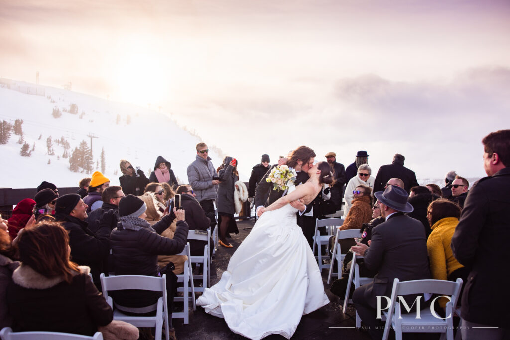 A bride and groom kiss and dip as they recess down the aisle as newlyweds at their rooftop mountain wedding ceremony in Mammoth.