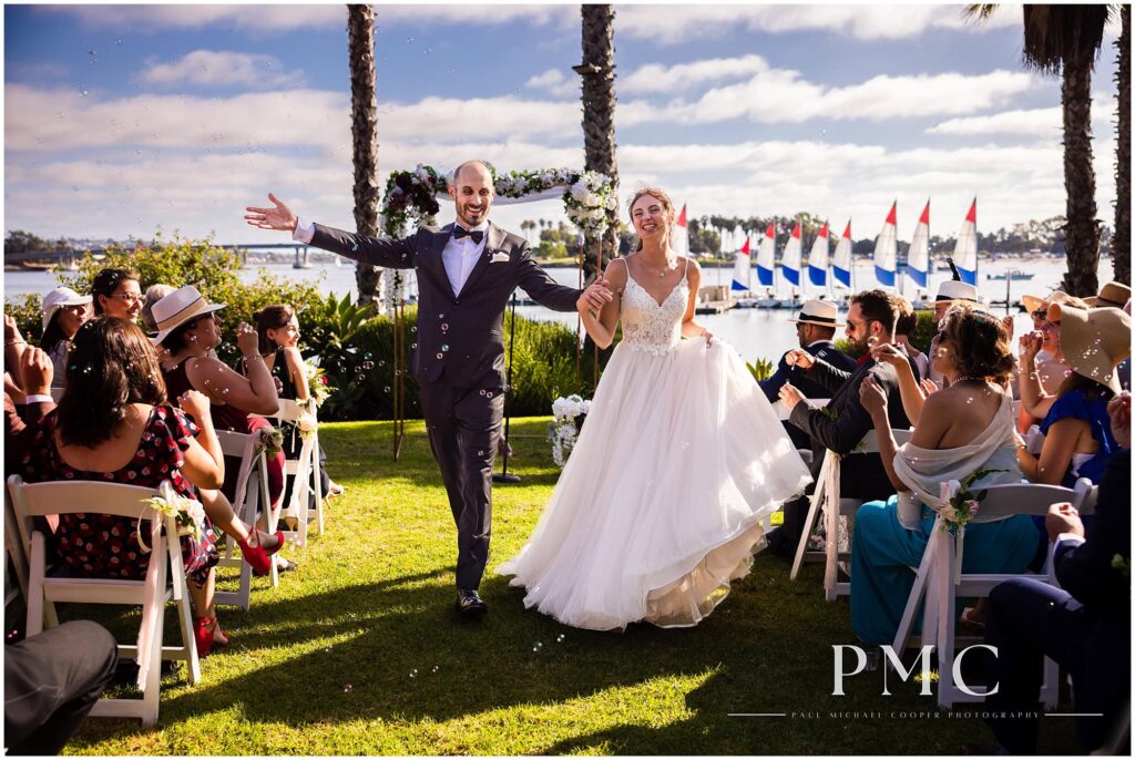 A bride and groom recess down the aisle during their ceremony at a waterfront wedding venue with a view of Mission Bay.