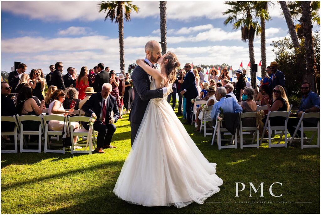 A bride and groom kiss at their ceremony at a waterfront wedding venue with a view of Mission Bay.