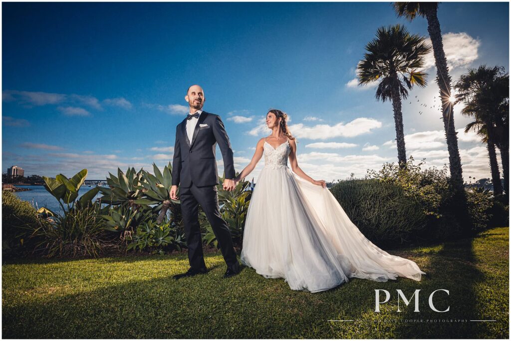 A bride and groom walk along the shore of the bay at a waterfront wedding venue.