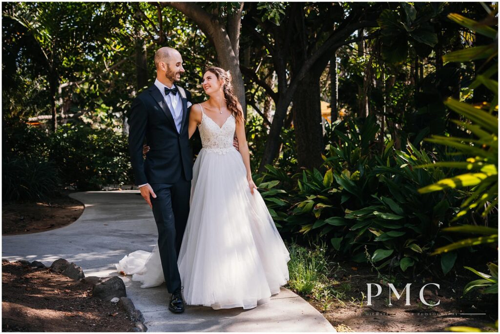 A bride and groom smile as they walk together through the gardens at Paradise Point Resort & Spa in Mission Bay.