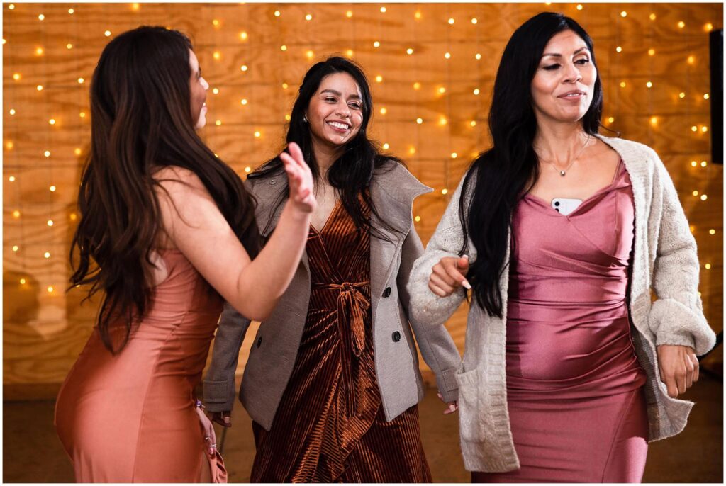 Guests at a fall wedding dance at the reception in rust and peach cocktail dresses with complementary coats.