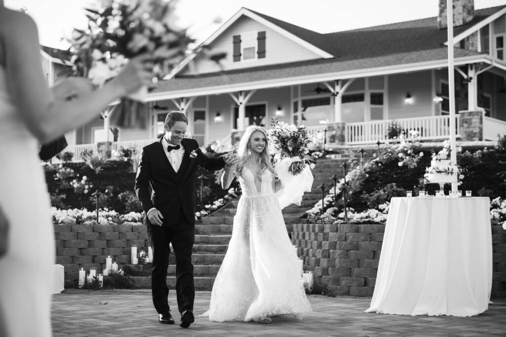 A black-and-white photo of a bride and groom entering their wedding reception hand-in-hand.