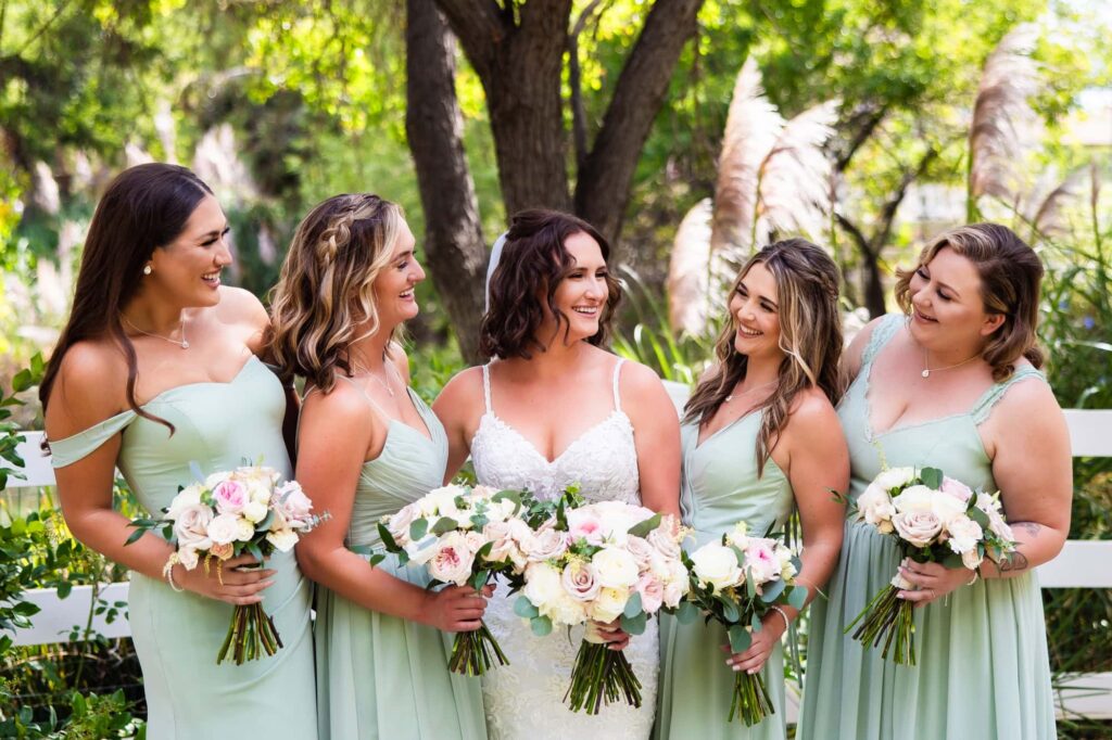 A bride and her bridesmaids smile at each other.