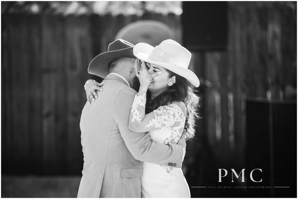 A bride and groom, both wearing boots and cowboy hats, share an emotional first dance during their reception on their country-style wedding day.