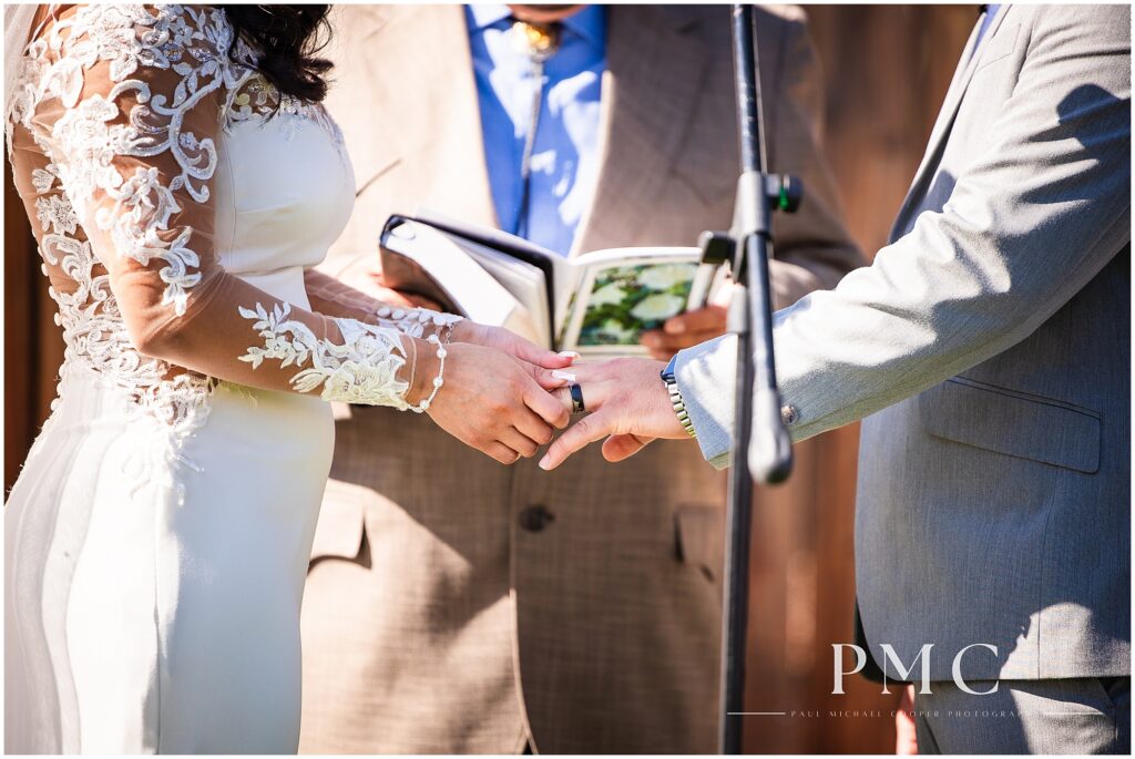 A close-up of a bride putting a custom country-style wedding ring on her groom's finger.