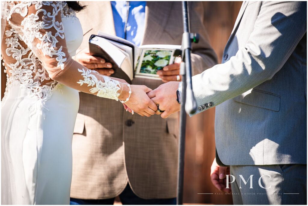 A close-up of a bride and groom's hands holding during their country-style outdoor ceremony.