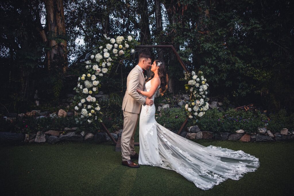 A bride a nd groom share an romantic embrace in front of their floral arch on their wedding day at Green Gables Estate.