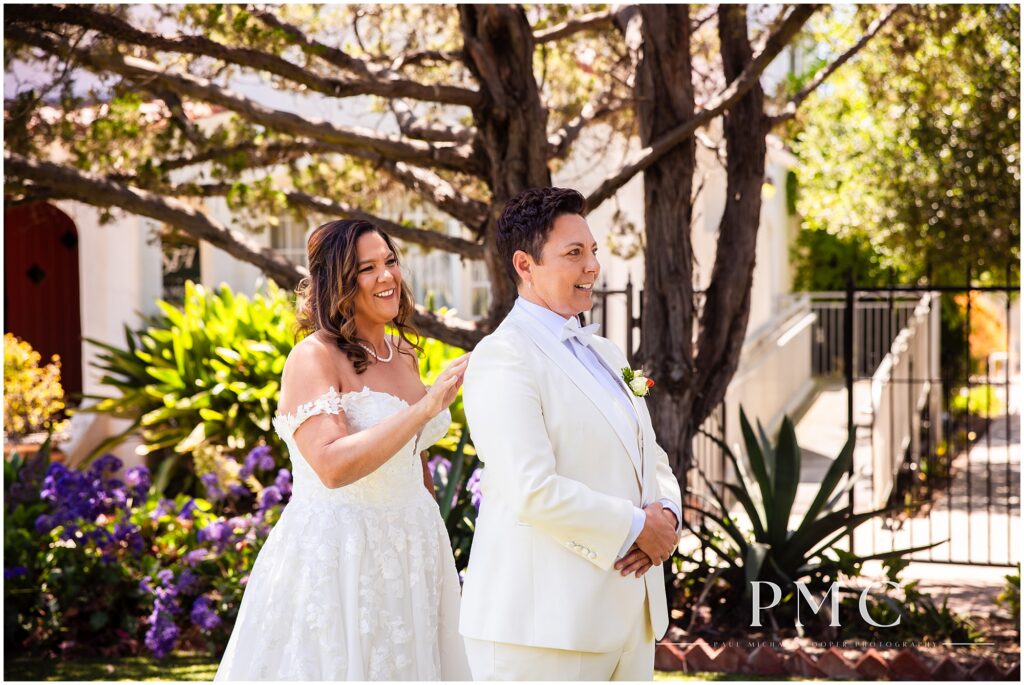 Two brides share a First Look moment on the front lawn of the terracotta, historical Rancho Minerva Wedding Venue in Vista.